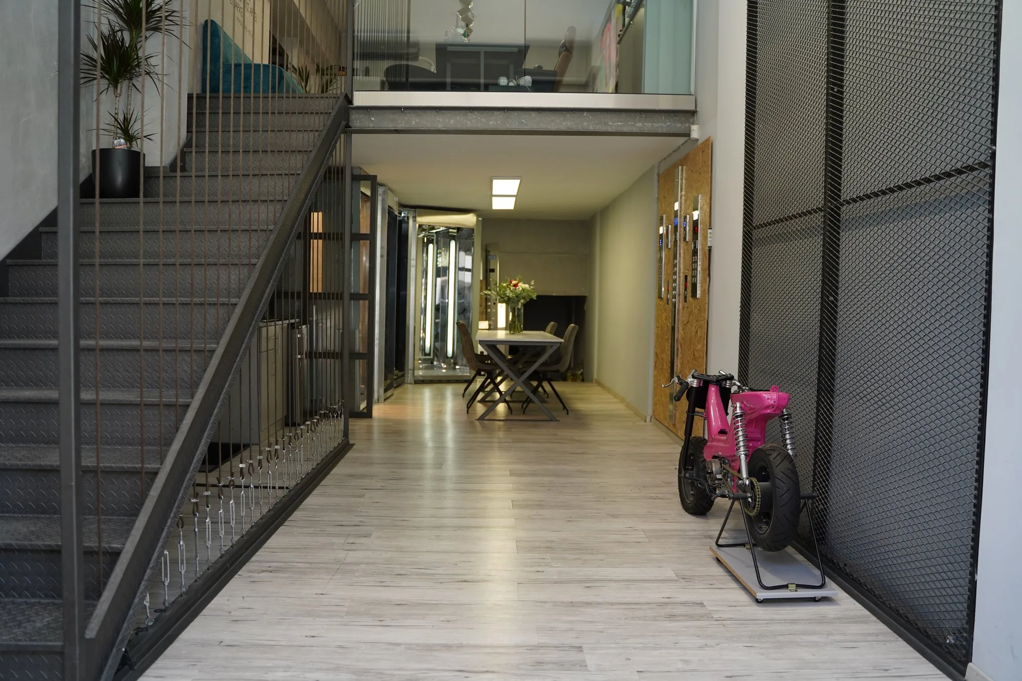 Το ισόγειο της Plexidas Elevators με τη μεταλλική σκάλα, το γυάλινο γραφείο στο πατάρι, πίνακες χειρισμού στον τοίχο και θαλάμους στο βάθος